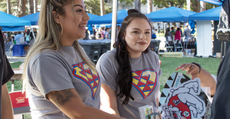 an image of two young women in matching t-shirts standing under an awning at some outdoor event
